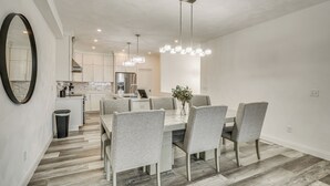 A modern kitchen with white cabinets, a stainless steel range, and a dining area with a marble countertop and grey upholstered chairs.