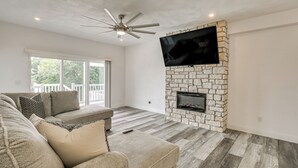 A living room with a stone fireplace, a ceiling fan, and a large window.