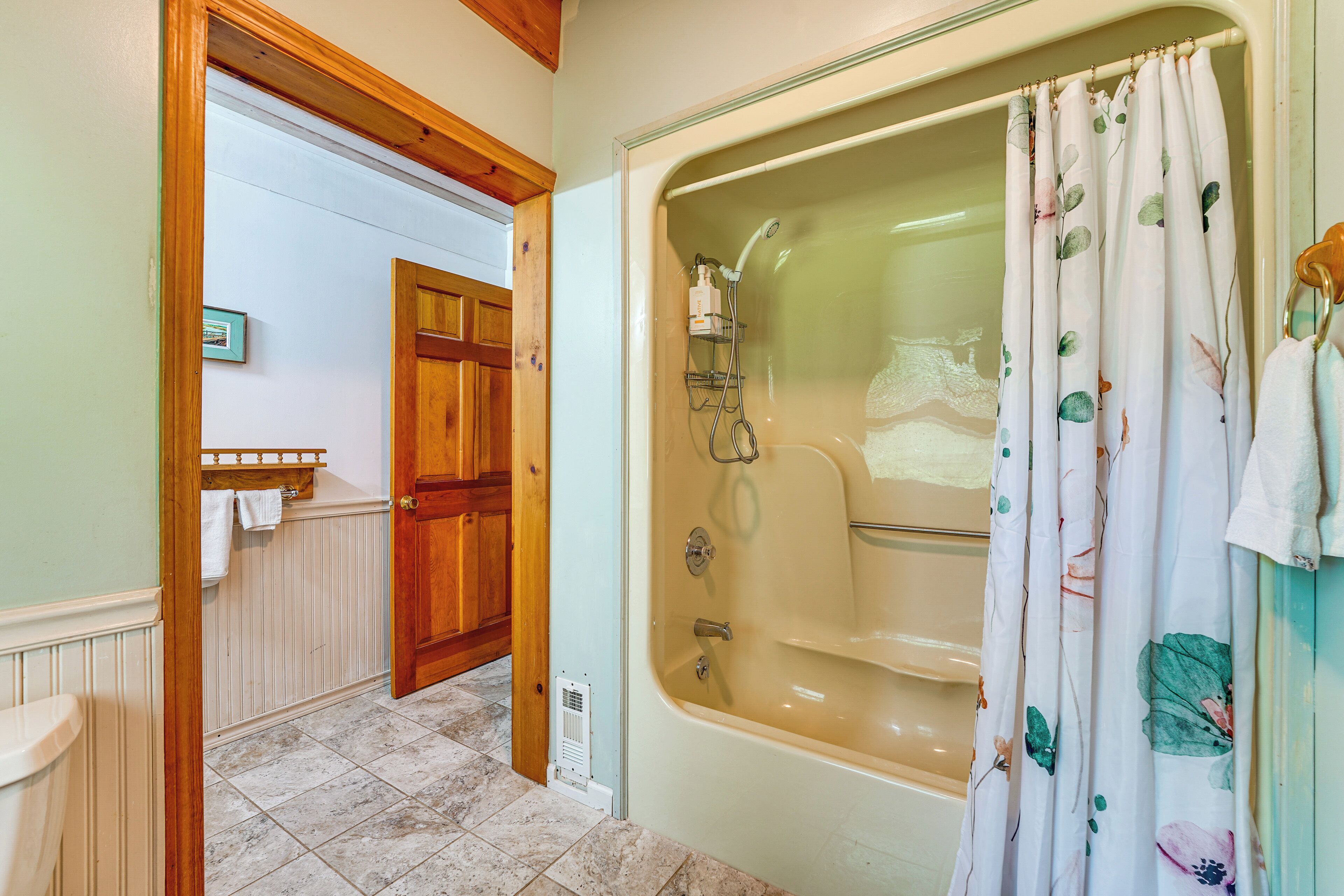 A bathroom with a bathtub, wooden door, and tiled floor.