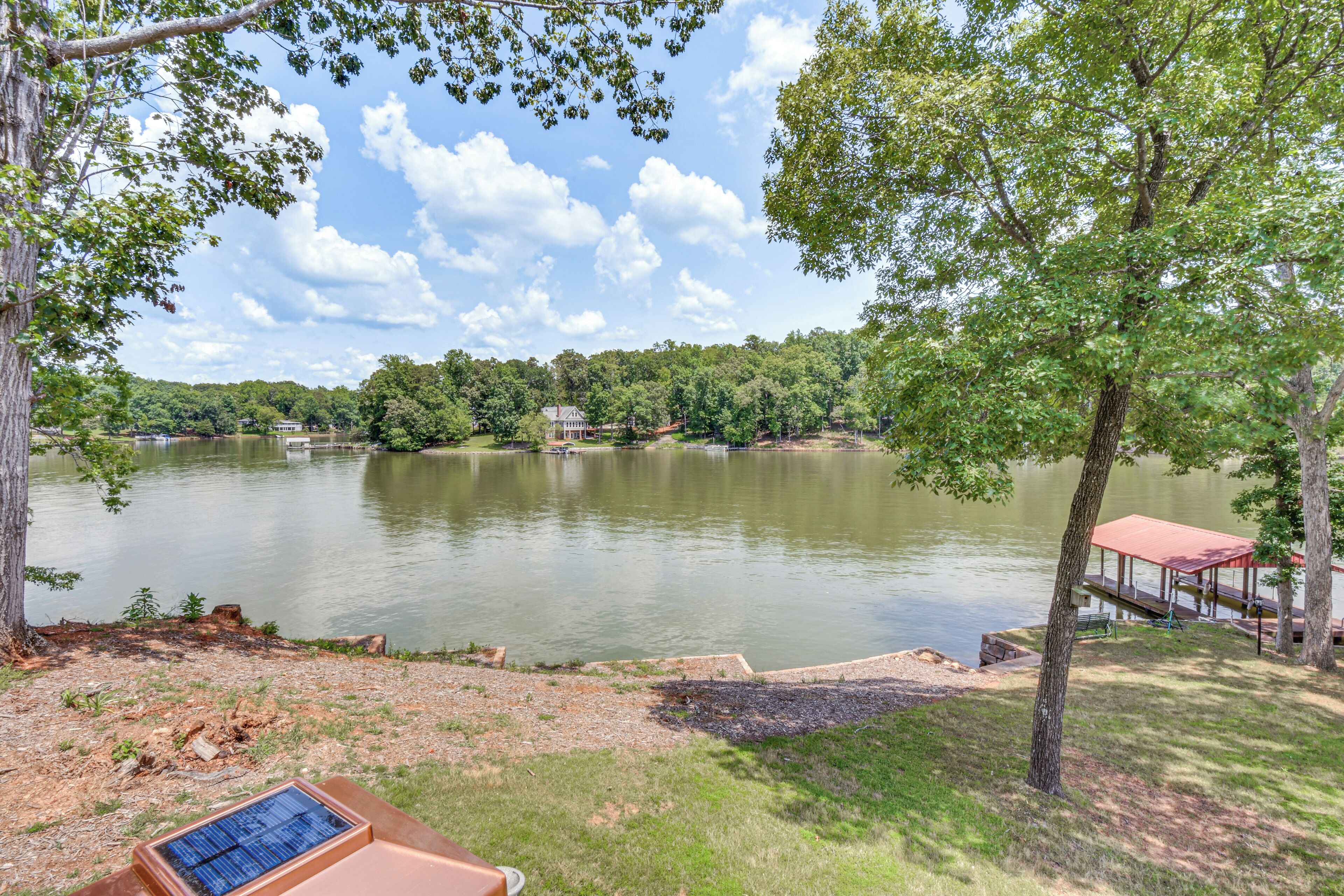 Une vue sur le lac, avec un quai, un espace pique-nique et une maison en arrière-plan.