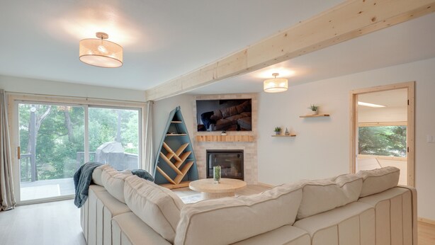 A modern living room with a sectional sofa, a fireplace, and a large window offering a view of the outdoors. - Lake Escape on Post Lake With Private Dock (Elcho)