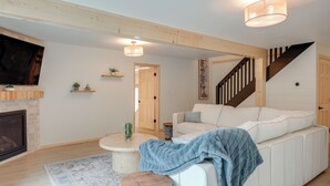A modern living room with a white sofa, a fireplace, a staircase, and a ceiling light fixture. - Lake Escape on Post Lake With Private Dock (Elcho)