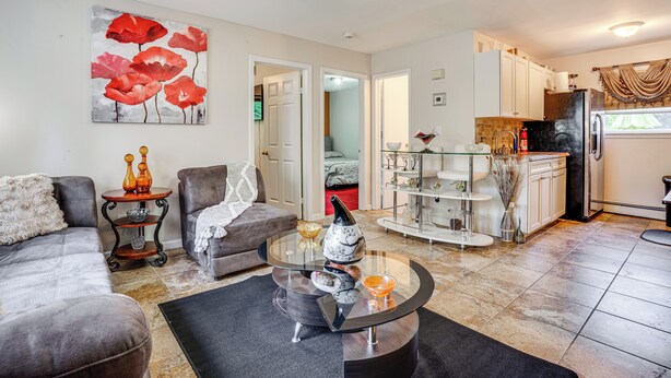 A modern living room with a glass coffee table, grey sofas, and a painting of red flowers. - 8 Mi to Long Beach: Cozy Apt w/ Fenced Yard! (Baldwin)