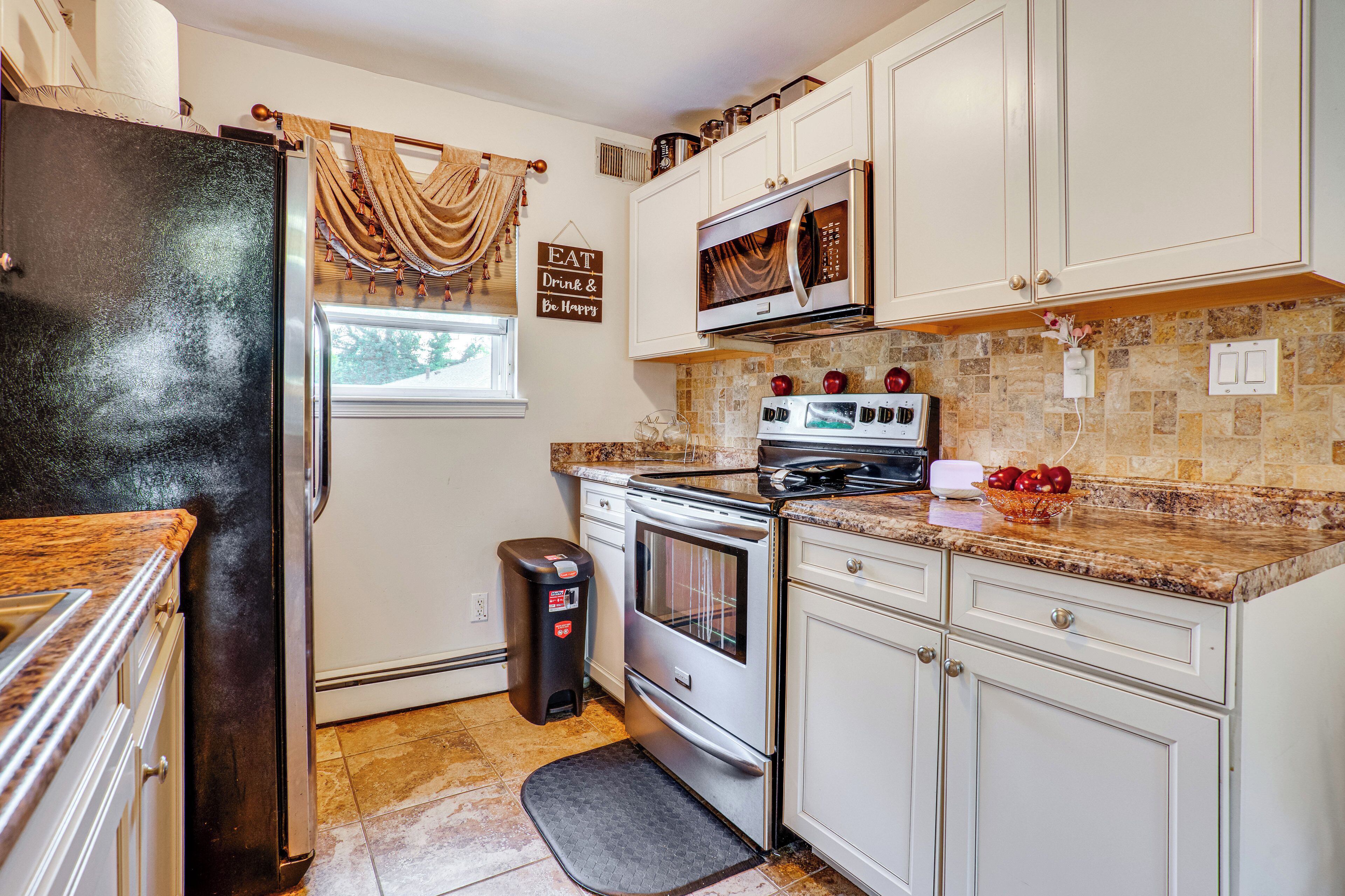 A kitchen with white cabinets, a stainless steel refrigerator, a microwave, an oven, and a trash can.