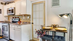A compact kitchen with white cabinets, a built-in microwave, and a dining area with a table set for two. - 8 Mi to Long Beach: Cozy Apt w/ Fenced Yard! (Baldwin)