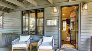 A wooden porch with two grey wicker chairs and a small table, a welcome mat, and a door leading inside. - Resort Perks, By Lake Glenville: Chinquapin Escape (Glenville)