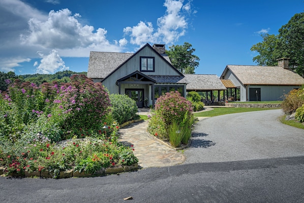 A two-story house with a stone pathway leading to the entrance, surrounded by well-maintained gardens and a clear blue sky.