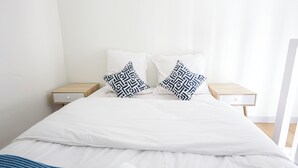 A neatly made bed with white bedding and two patterned pillows, flanked by wooden nightstands with drawers. - Appart'hotel Cannes Sun (Cannes)