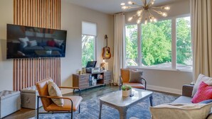 A modern living room with a flat-screen TV, a guitar, a coffee table, and a sofa. - Ultimate Rooftop Double Games BBQ Skyline Views (Nashville)