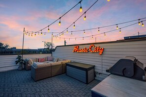 An outdoor patio area with string lights, a sofa, a grill, and a neon sign that reads "Music City". - Ultimate Rooftop Double Games BBQ Skyline Views (Nashville)