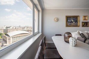 A modern living room with a large window, a dining table, and a sofa. - Views of all the Palaces 2BR Stunner (Bucharest)
