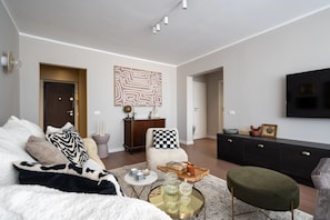 A modern living room with a sofa, armchair, coffee table, and a flat-screen TV mounted on the wall. - Views of all the Palaces 2BR Stunner (Bucharest)