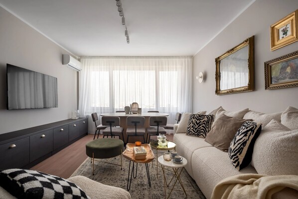 A modern living room with a sofa, coffee table, and a dining area with chairs and a table. - Views of all the Palaces 2BR Stunner (Bucharest)