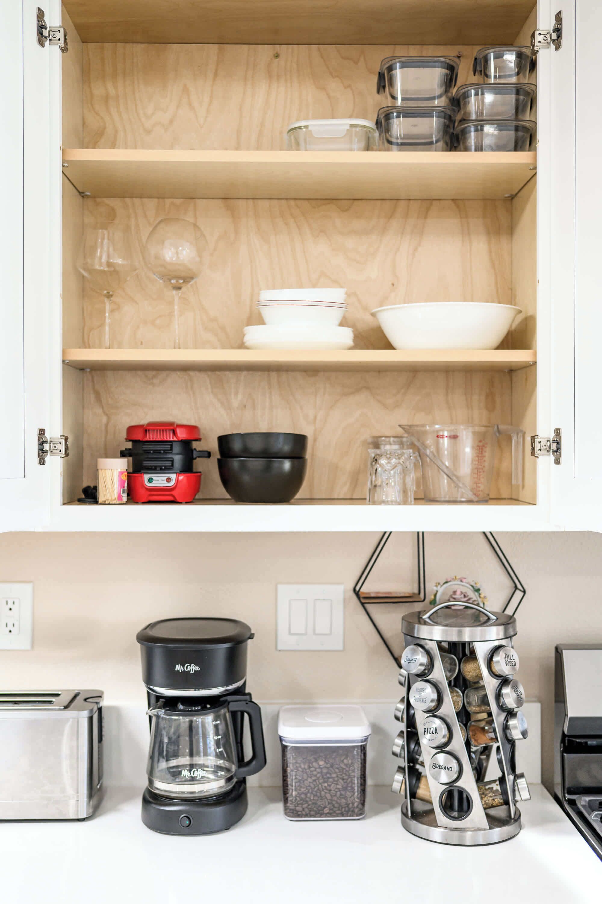 A kitchen with a wooden cabinet containing various kitchenware, a coffee maker, a toaster, and a spice rack.