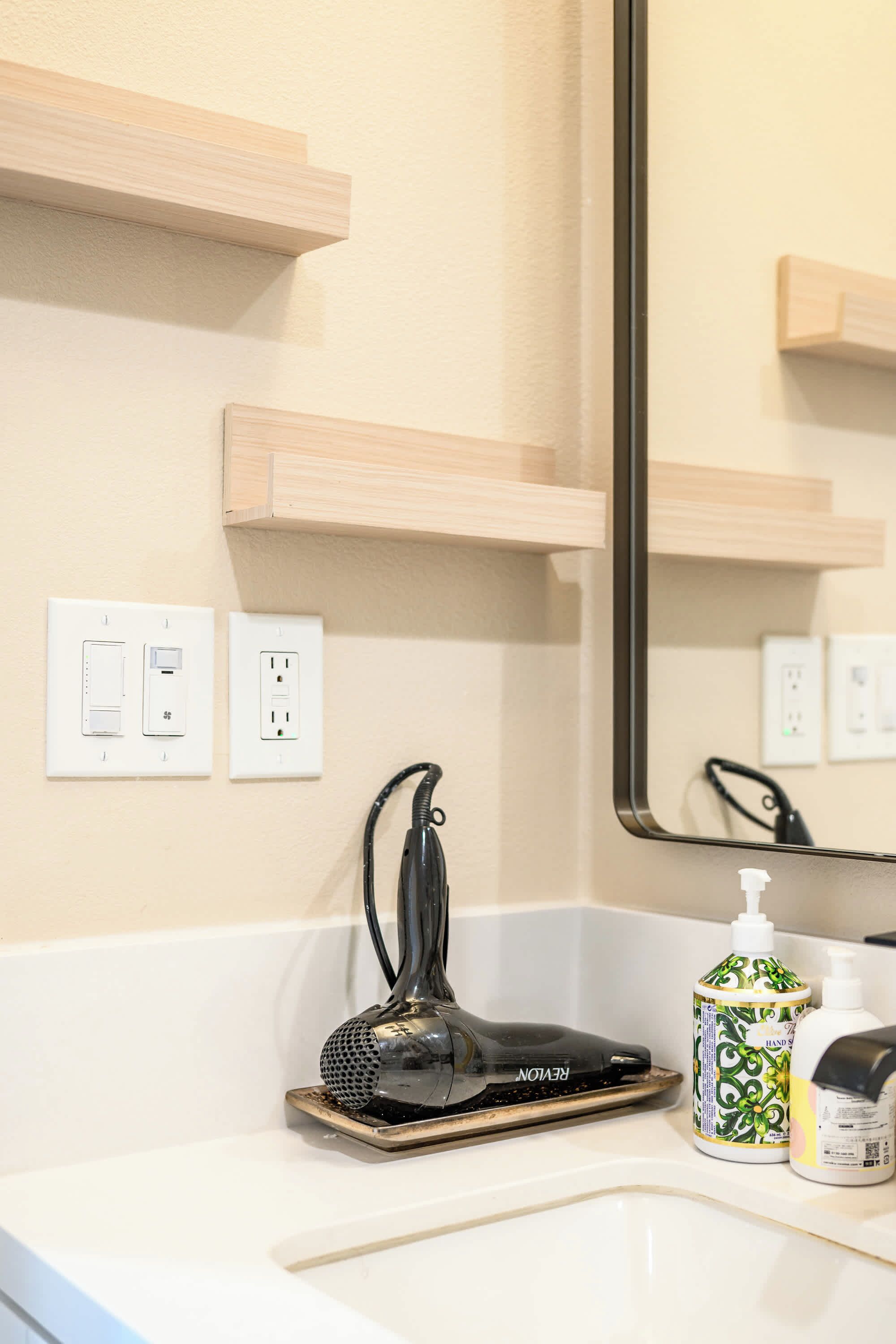 A bathroom with a white sink, a mirror, a hairdryer, and two bottles of hand soap.