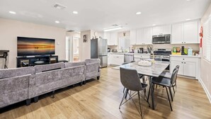 A modern kitchen with white cabinets, a dining area with a marble table, and a gray sofa.