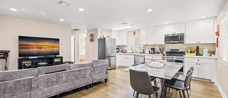 A modern kitchen with white cabinets, a dining area with a marble table, and a gray sofa.