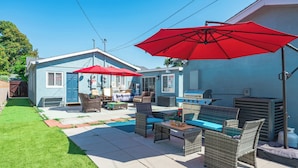 A backyard with outdoor furniture, a barbecue grill, and a large red umbrella.
