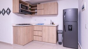 A compact kitchen with wooden cabinets, a built-in microwave, a gas stove, a sink, and a refrigerator.