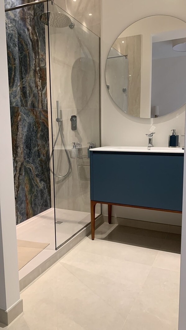 A modern bathroom with a glass-enclosed shower, a round mirror, and a dark blue vanity.