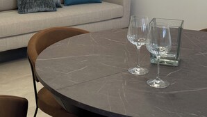 Una sala de estar moderna con una mesa redonda de mármol, dos copas de vino, un sofá beige con un cojín azul, y una lámpara de pared.