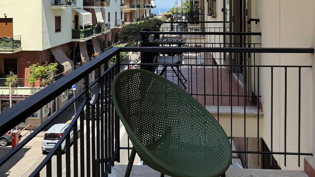 Un balcón con una silla verde, barandilla y vistas a edificios cercanos.