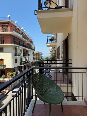 A balcony with a green chair, a railing, and a view of adjacent buildings.