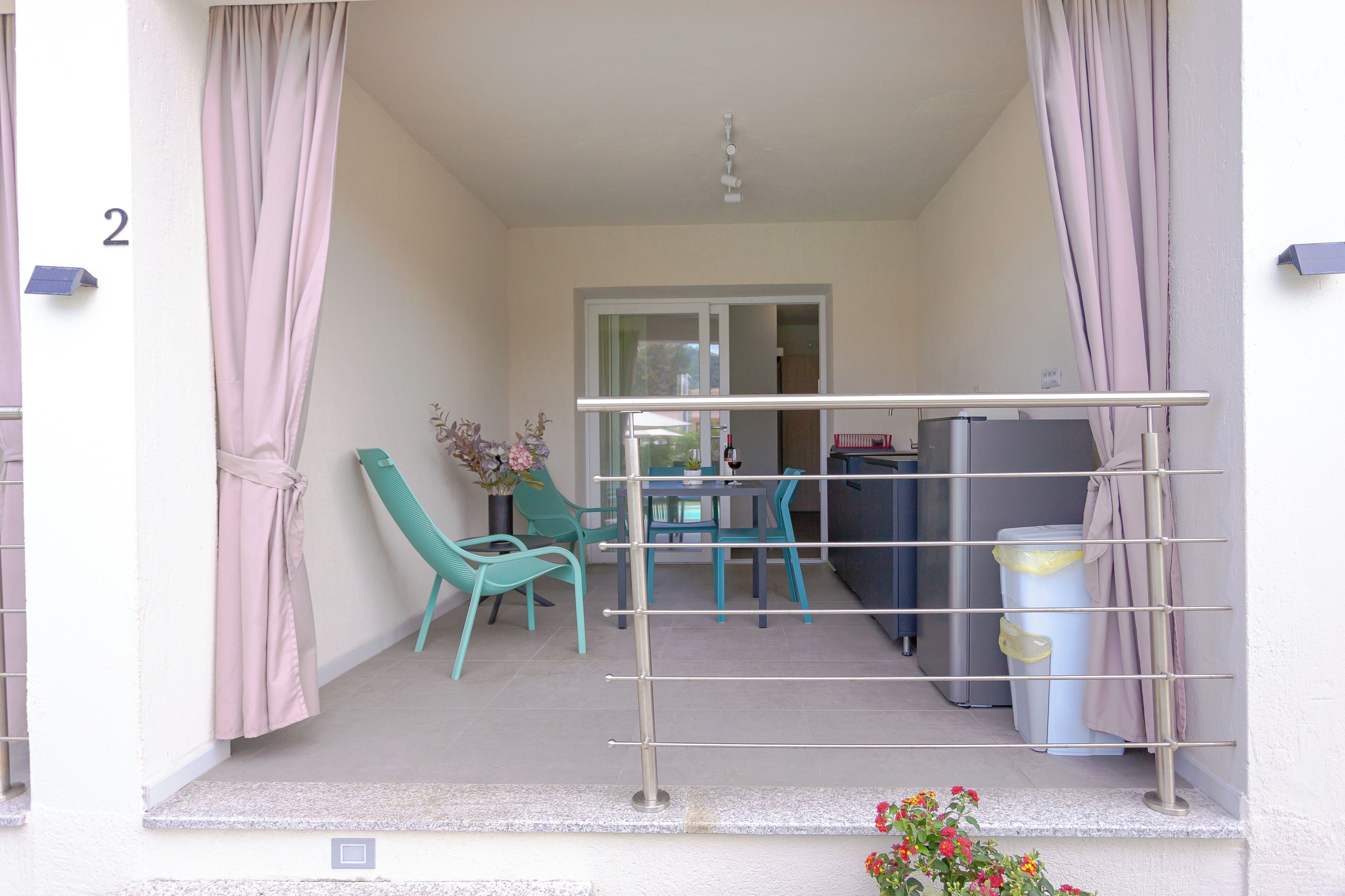 A balcony with a metal railing, a table with chairs, a trash bin, and a door leading to an indoor area.