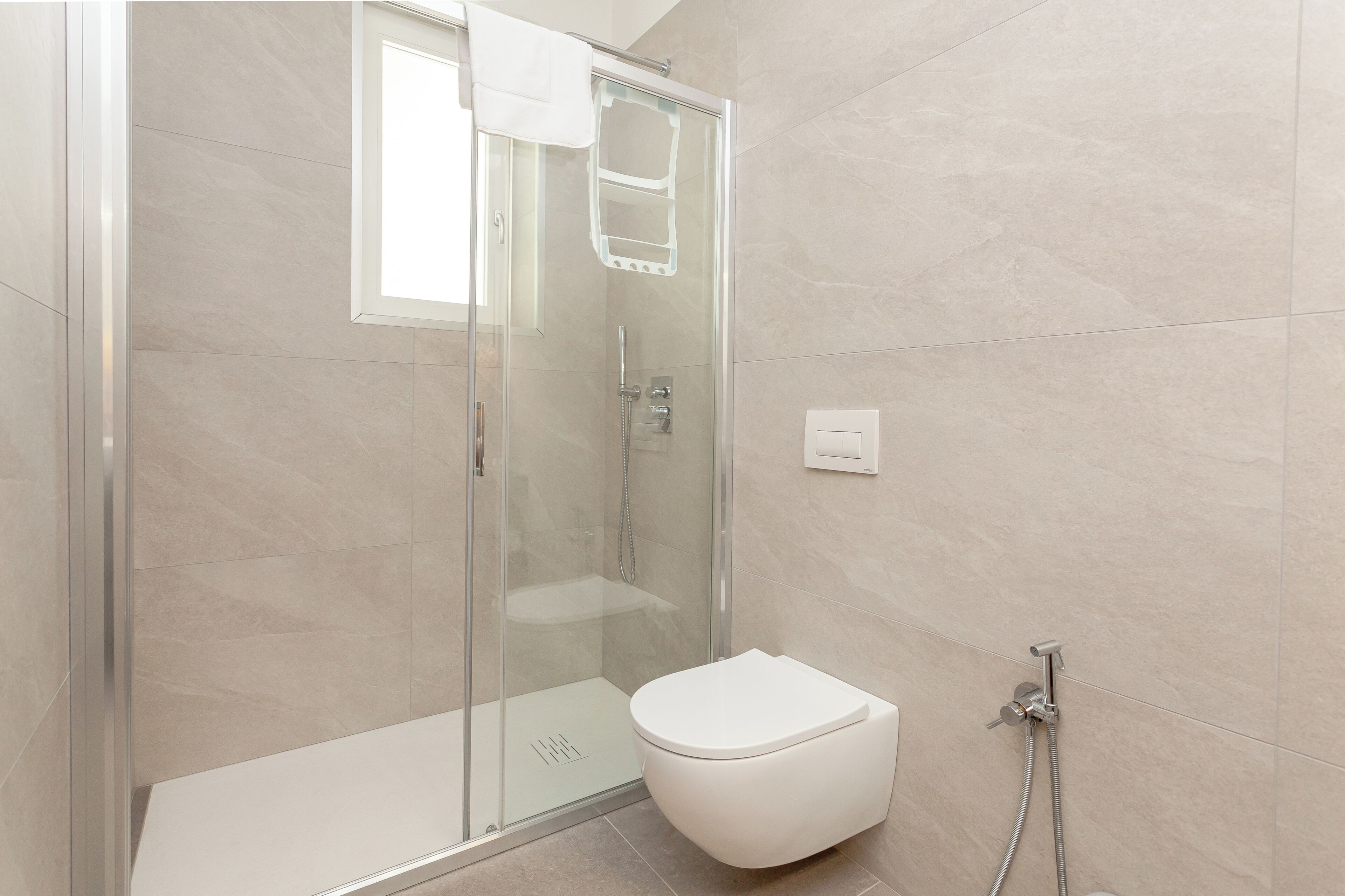 A modern bathroom with a glass-enclosed shower, a white toilet, and a handheld showerhead.