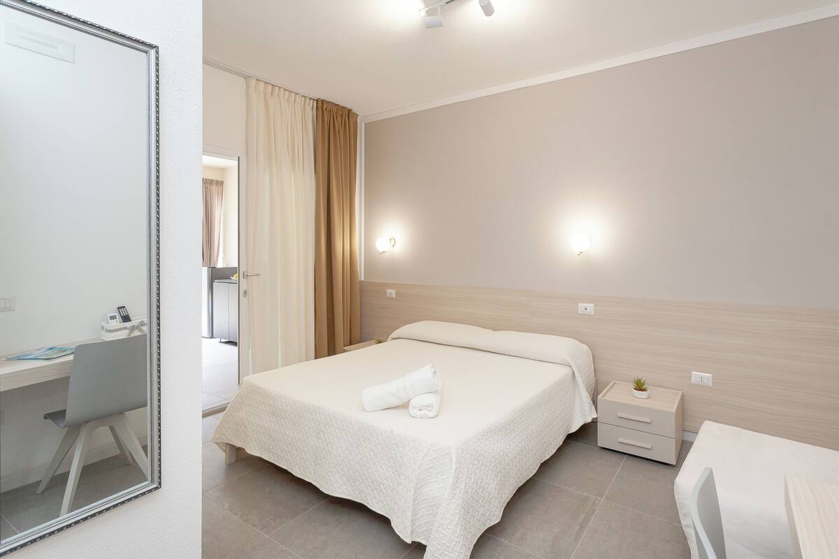 A hotel room with a bed, bedside table, and a desk with a chair.