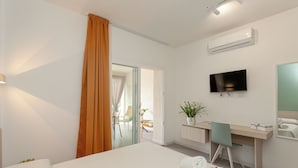 A hotel room with a bed, a desk, a chair, a TV, and an air conditioning unit.