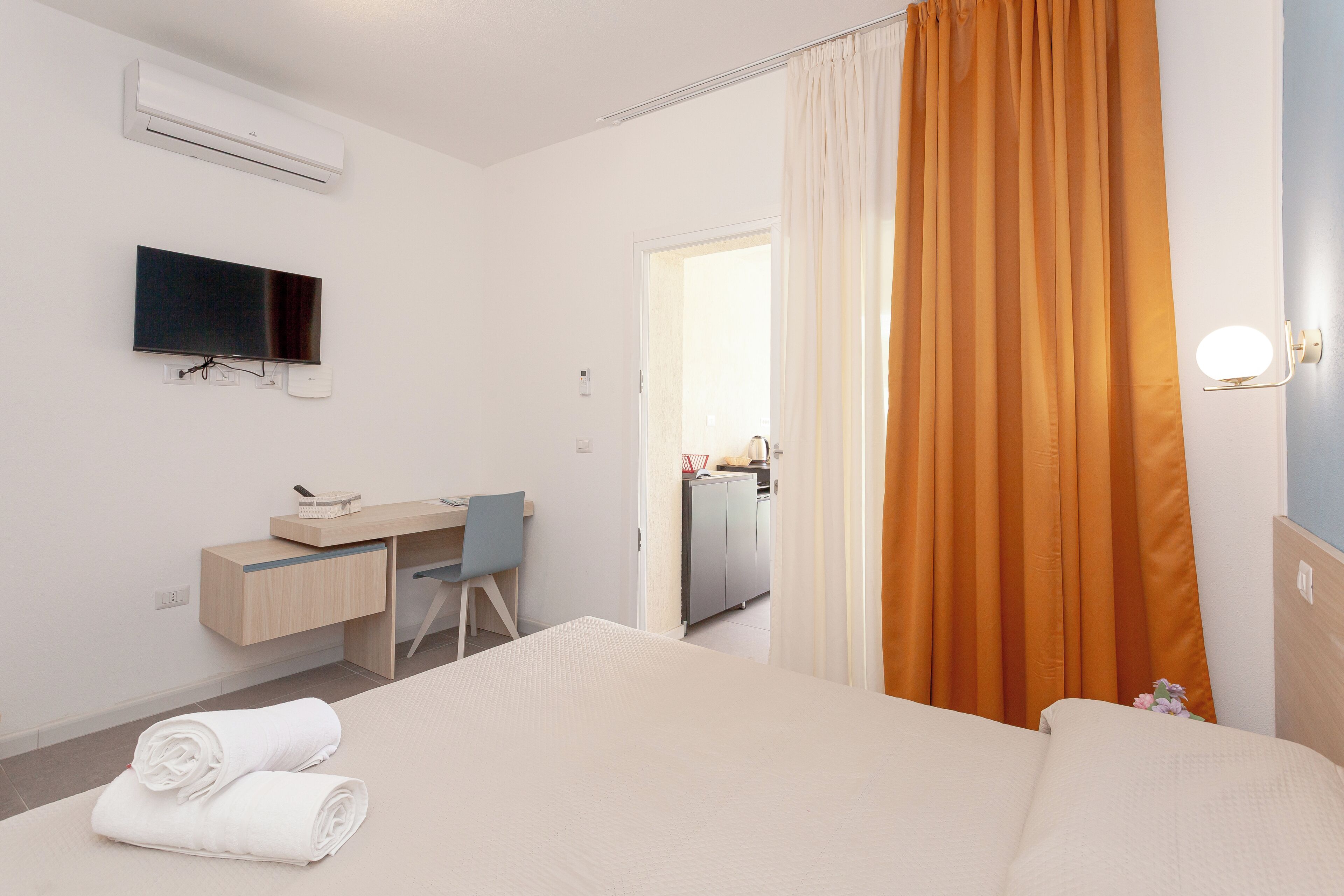 A hotel room with a bed, a desk, a chair, a TV, and a bathroom visible through an open door.