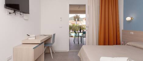 A hotel room with a bed, a desk, a TV, and a view of an outdoor pool area.