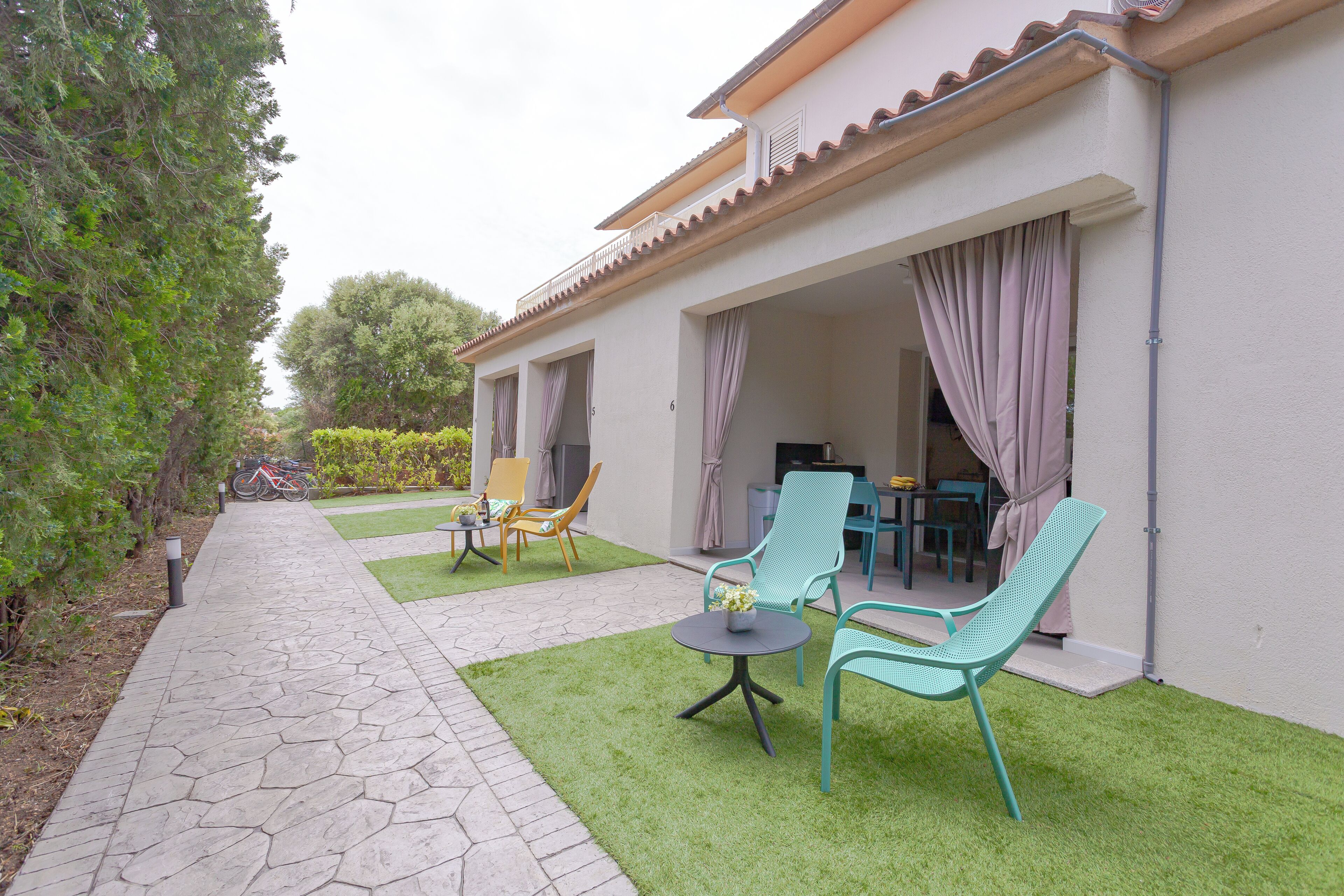 A patio with green artificial grass, two chairs, a small table, and a bicycle.