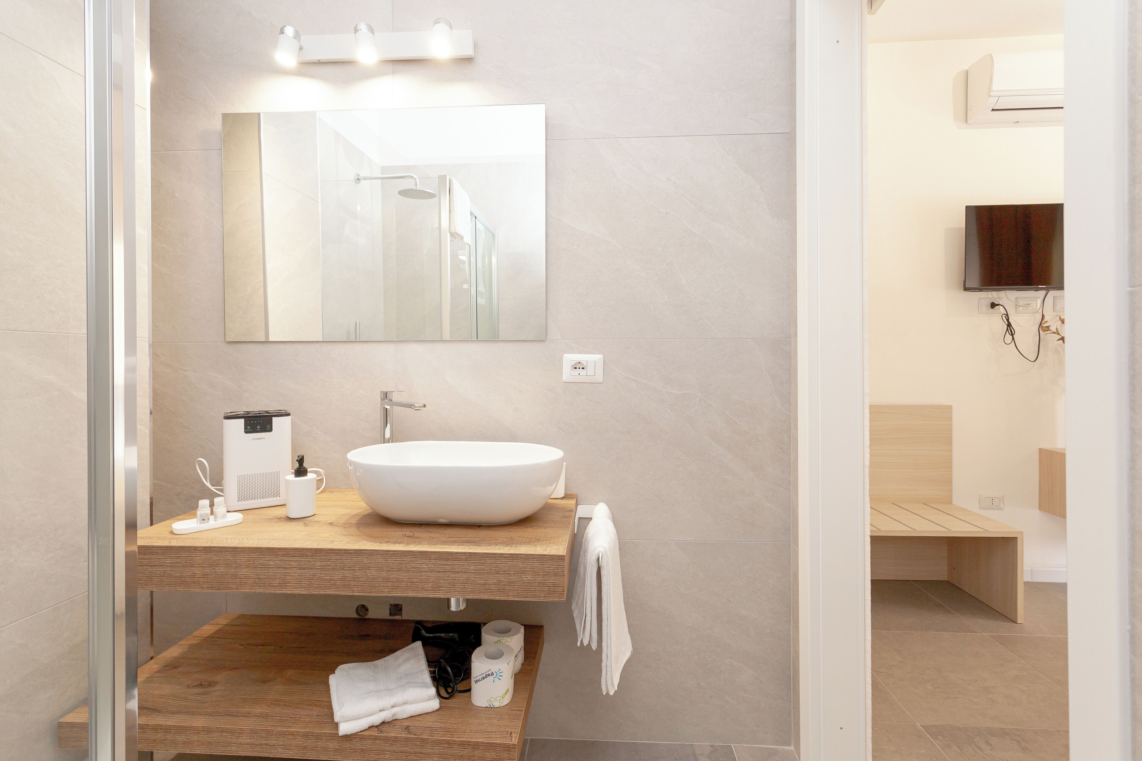 Une salle de bain moderne avec un grand miroir, un lavabo sur colonne, un meuble-lavabo en bois, un porte-serviettes et un espace douche.