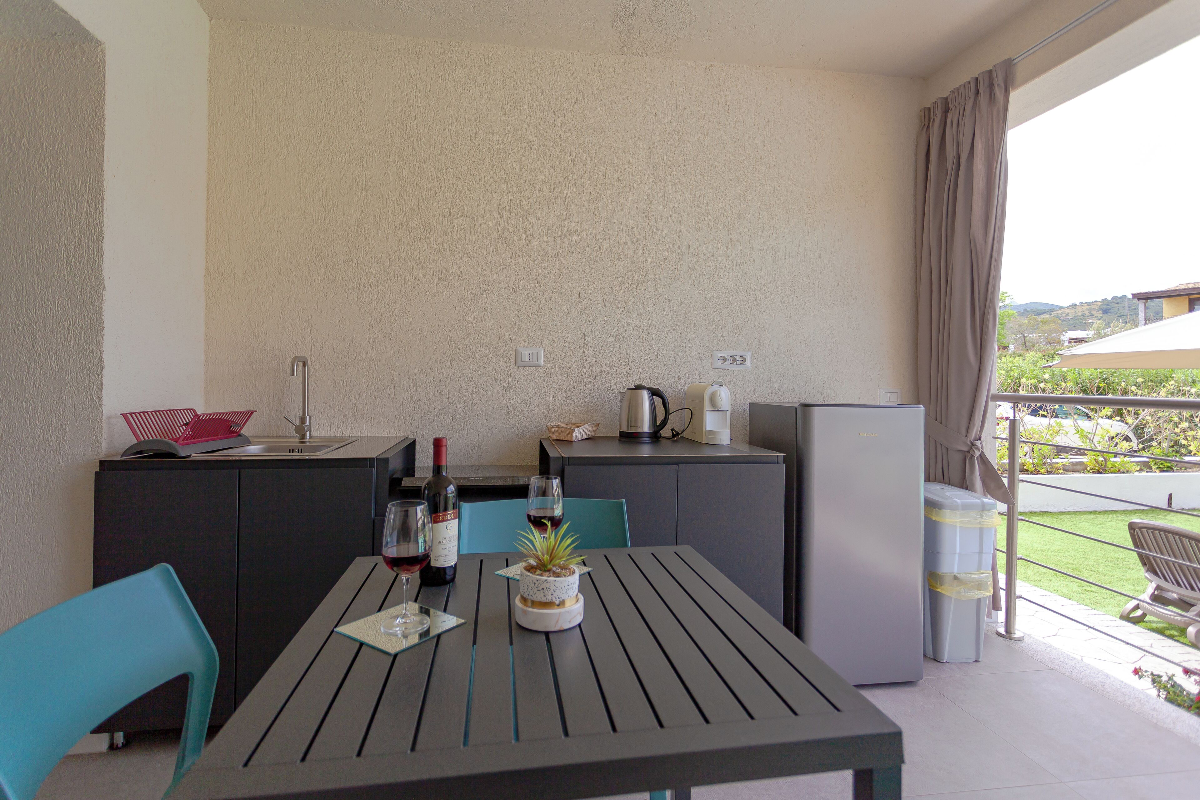 A balcony with a table, chairs, a refrigerator, and a view of the outdoors.