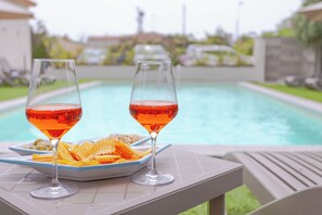 Two glasses of red drink on a table by a pool with a plate of chips. - Le dune RELAX camere cucina&piscina (San Teodoro)