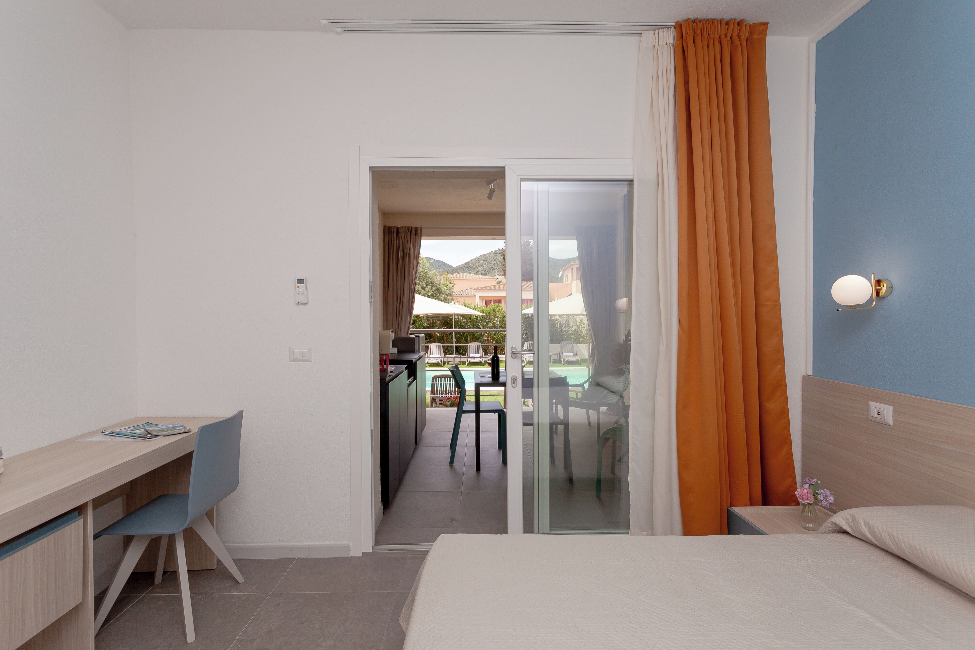 A hotel room with a bed, a desk, and a view of an outdoor dining area.