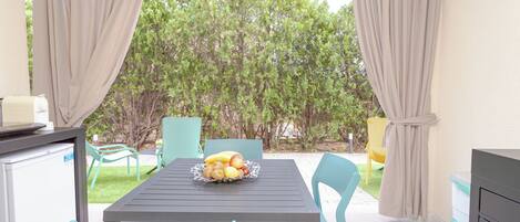A patio with a table and chairs, a fruit bowl, and a refrigerator.