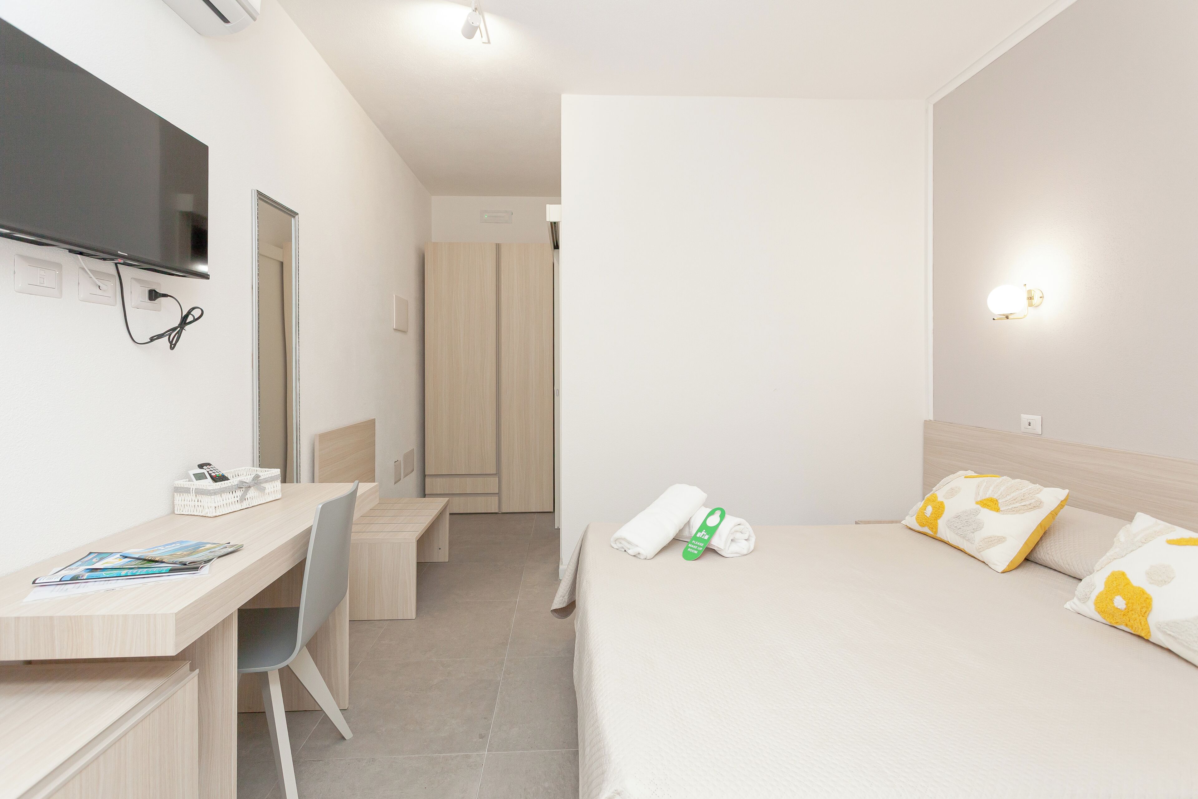 Una camera d'albergo con scrivania, sedia, letto e televisore montato a parete.