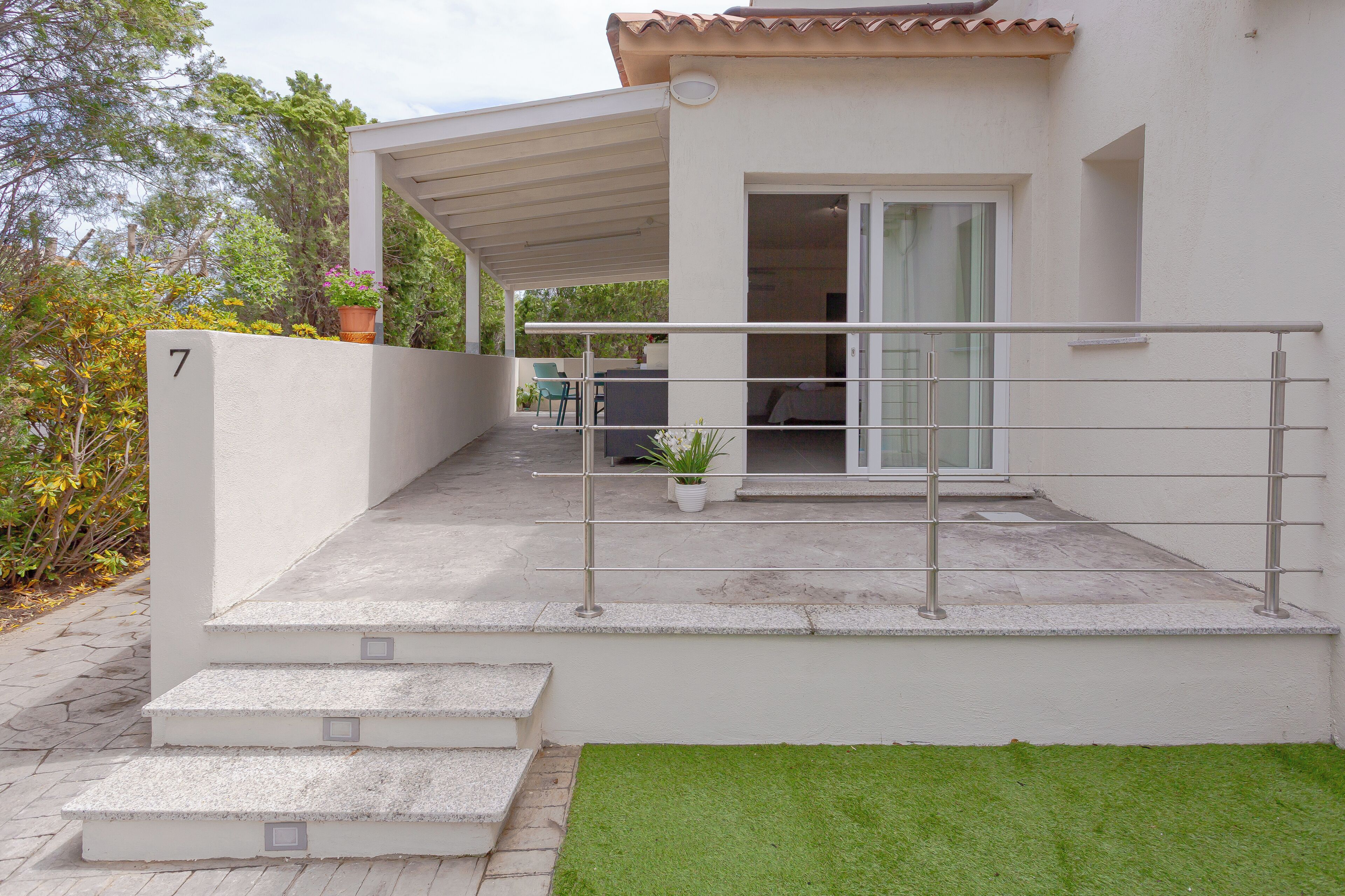 A modern house with a covered patio, a set of steps leading to the entrance, and a number '7' on the wall.