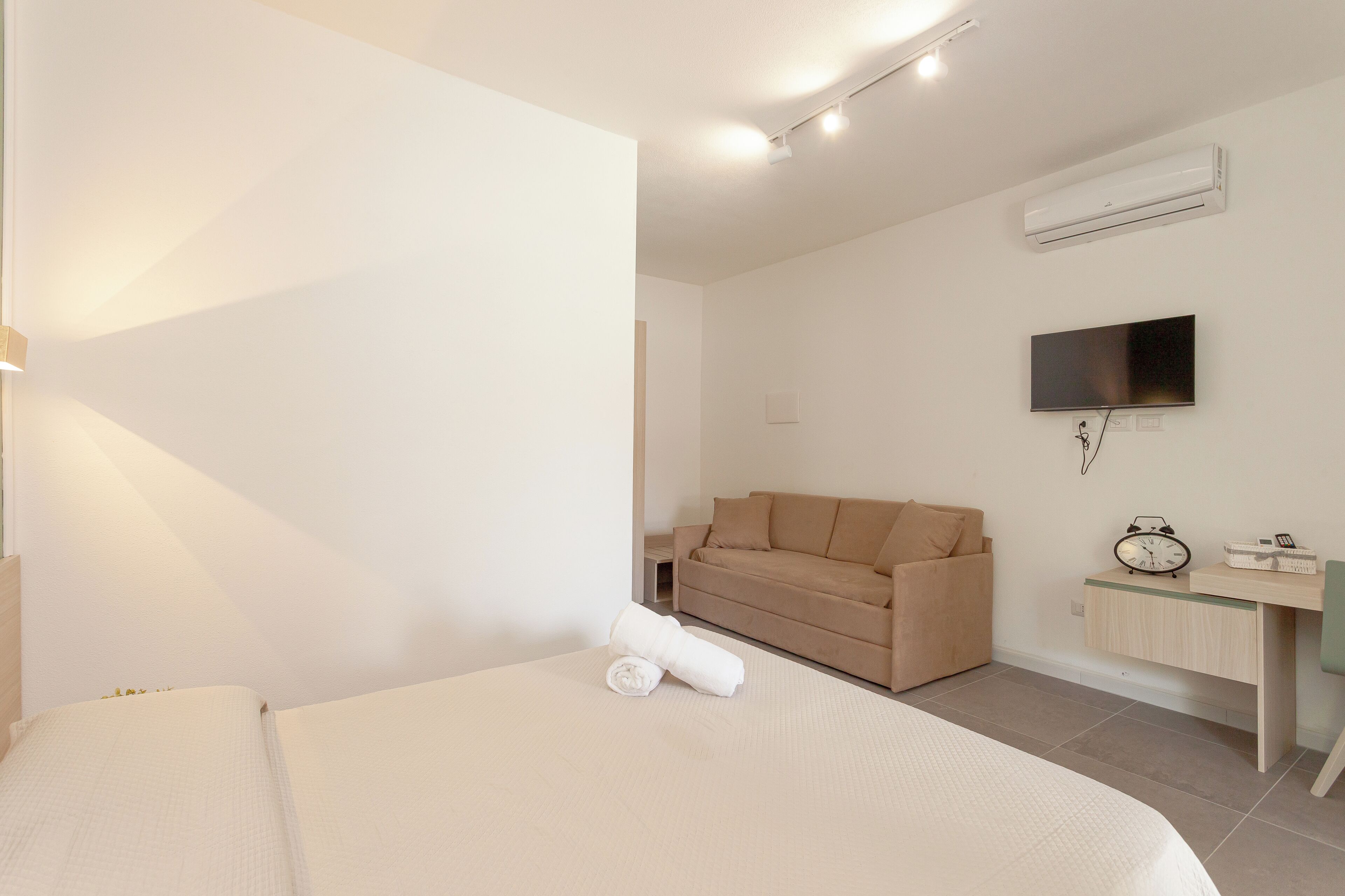 Quarto de hotel moderno com cama, sofá, escrivaninha e televisão de tela plana, além de ar condicionado.