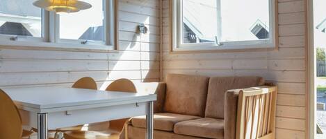 Ein Zimmer mit einem weißen Tisch und Stühlen, einem braunen Sofa und zwei Fenstern mit Jalousien.