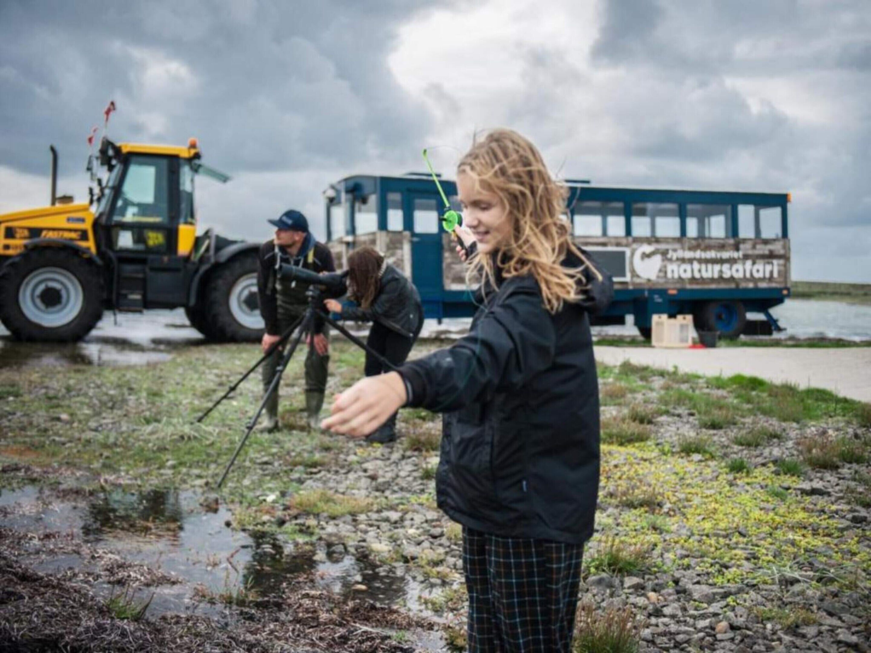 A person with a camera on a tripod, a vehicle with 'naturafahrt' written on it, and a tractor in the background.