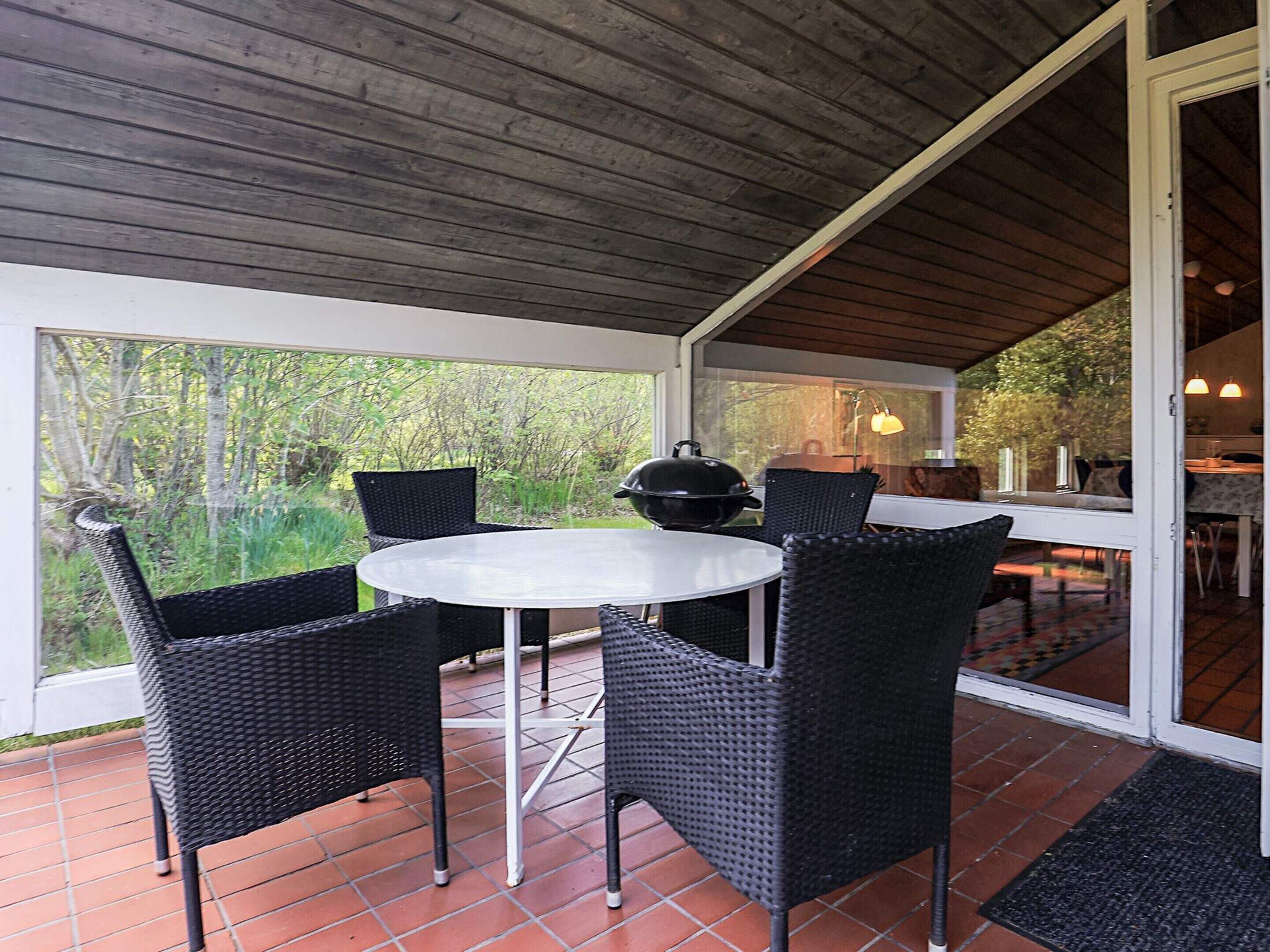 Un patio al aire libre con una mesa redonda y cuatro sillas, una parrilla y vistas a zonas verdes.