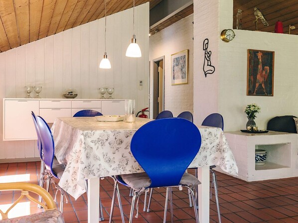 Un comedor con una mesa dispuesta para seis personas, rodeado de sillas azules, un armario blanco con puerta de cristal y un cuadro en la pared.