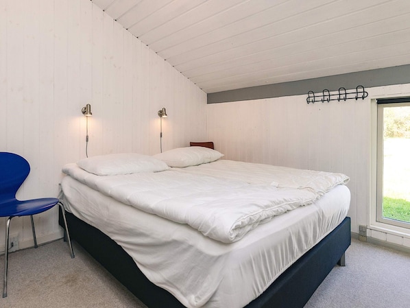 A bedroom with a bed, two wall-mounted lamps, a blue chair, and a window.