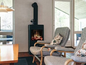 A room with a wood-burning stove, two upholstered chairs with floral cushions, and a wooden table. - 6 Person Holiday Home in Jerup (Jerup)