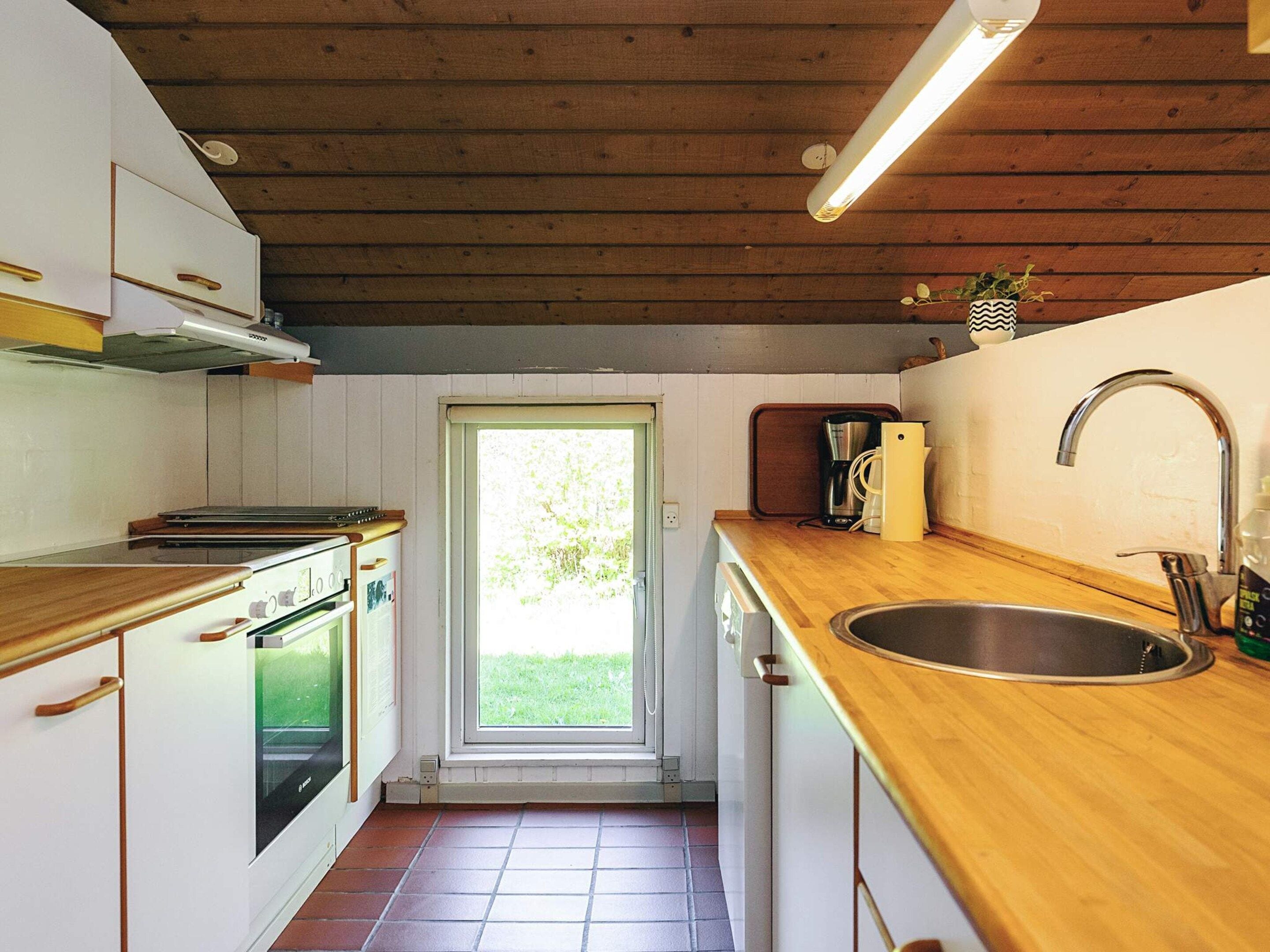 Cocina compacta con armarios de madera, un lavamanos de acero inoxidable y un ventanal que proporciona luz natural.