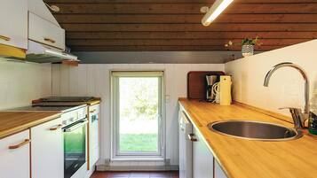 Cocina compacta con armarios de madera, un lavamanos de acero inoxidable y un ventanal que proporciona luz natural.